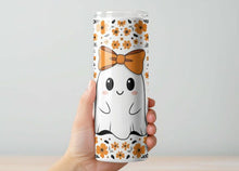 Load image into Gallery viewer, A hand holding a tall insulated tumbler with a white ghost character wearing an orange bow, surrounded by small orange flowers on a white background.
